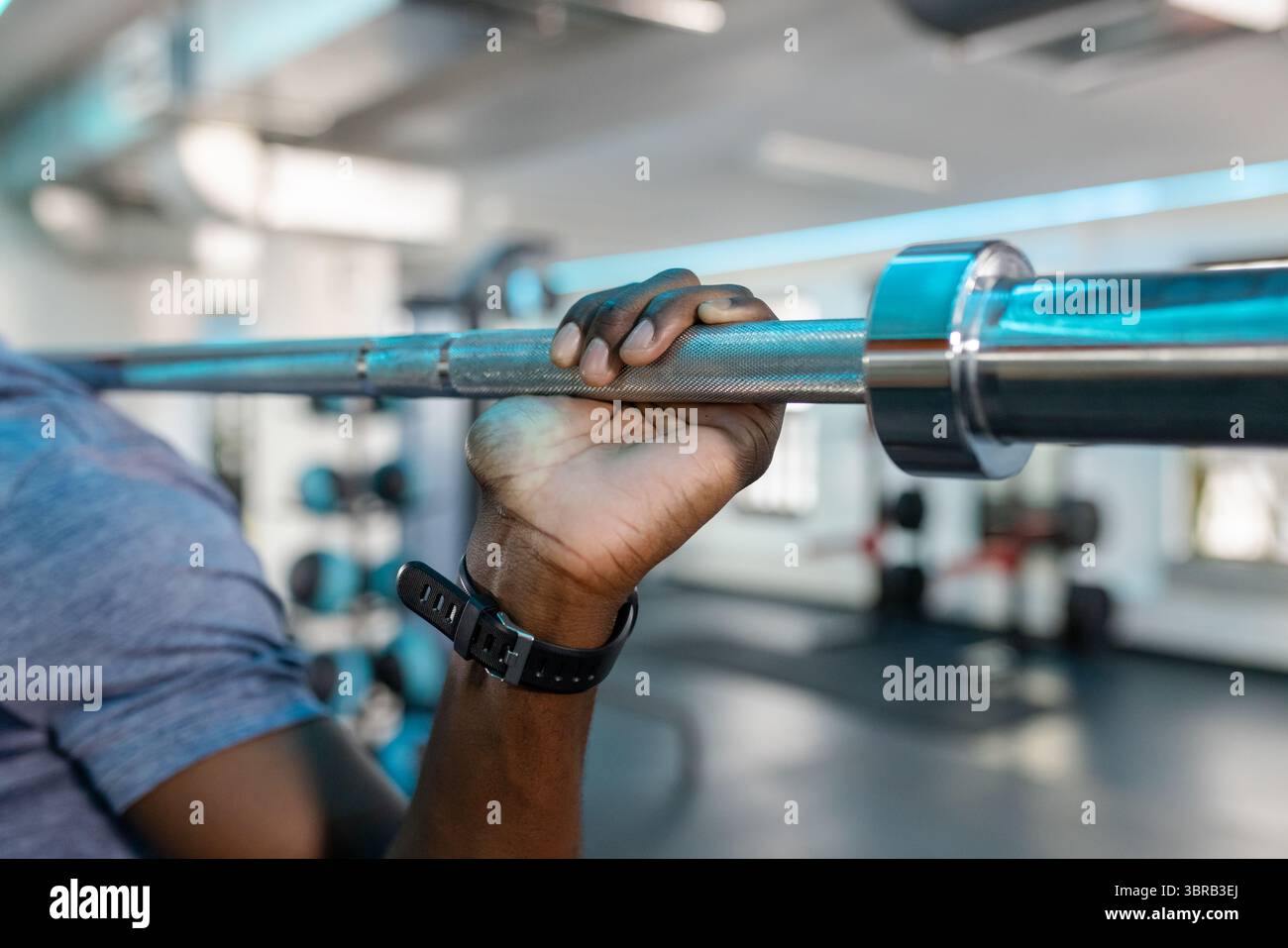 Uomo afro-americano che si prende il barbell olimpico in palestra mostrando collare zigrinato e smartwatch Foto Stock
