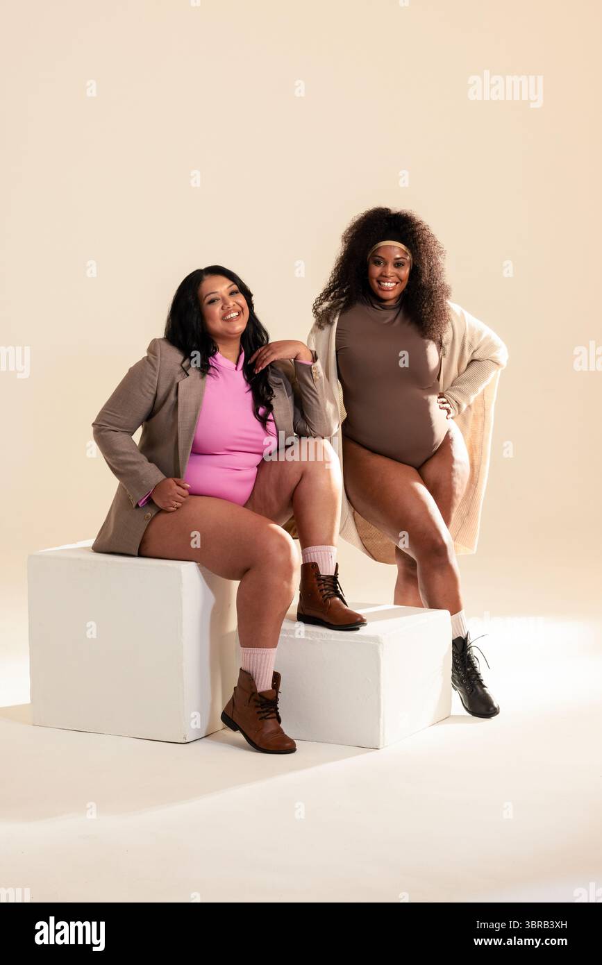 Diverse amiche che posano in studio fotografico su blocchi bianchi indossando tute Foto Stock