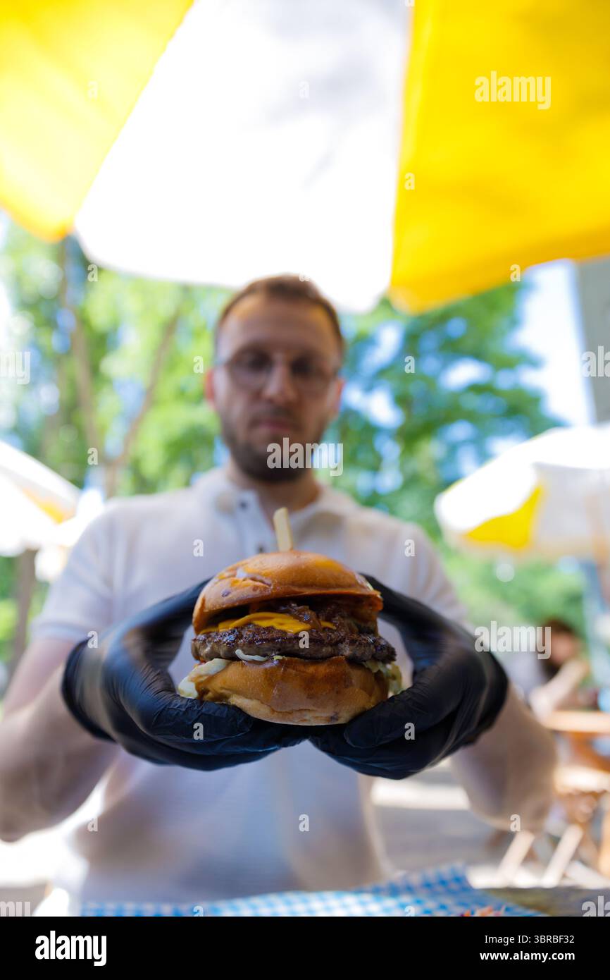 Delizioso hamburger artigianale esposto dallo chef, con ingredienti freschi e gustosi condimenti sotto il baldacchino luminoso all'aperto in una cucina vivace Foto Stock