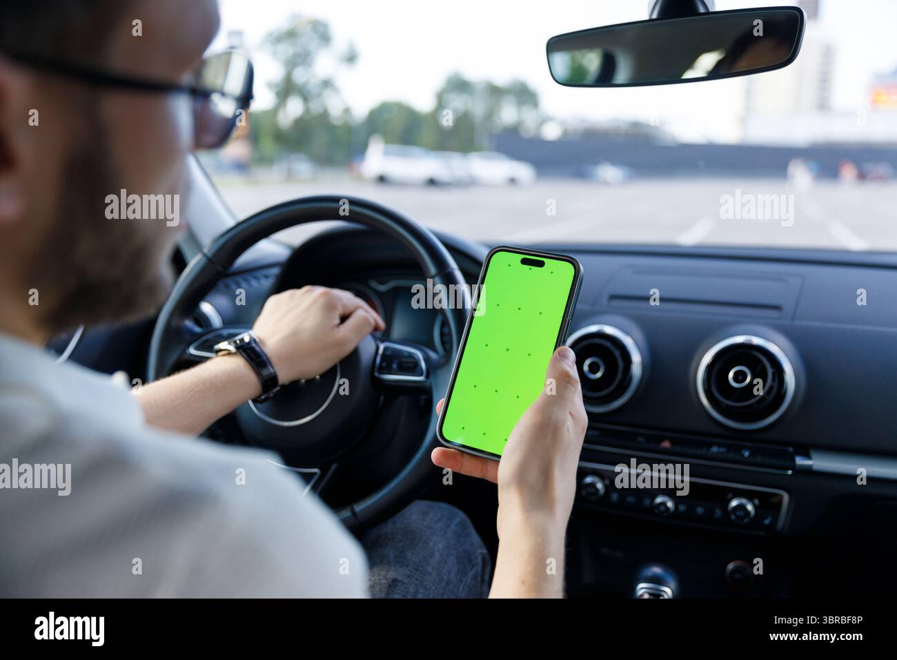 Un uomo all'interno di un'auto che utilizza uno smartphone con un vivace schermo verde, che mostra l'intersezione tra tecnologia e guida in un ambiente urbano moderno Foto Stock