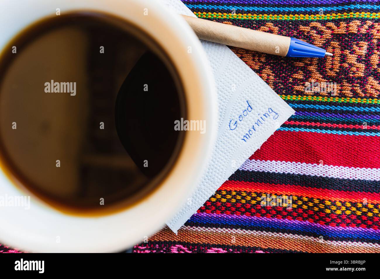 Tazza di caffè con una nota che dice Buongiorno su un tavolo colorato con intreccio Inca. Foto Stock