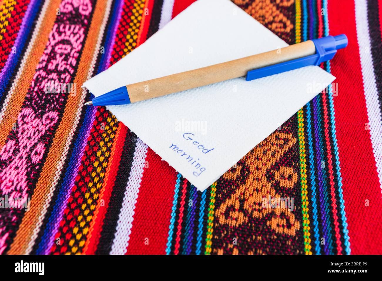 Tazza di caffè con una nota che dice Buongiorno su un tavolo colorato con intreccio Inca. Foto Stock