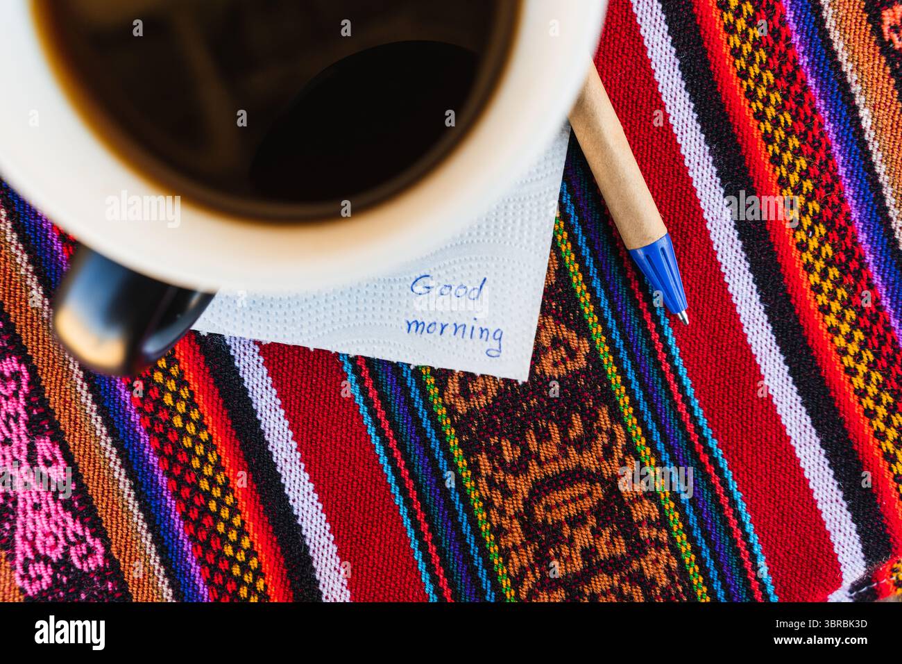 Tazza di caffè con una nota che dice Buongiorno su un tavolo colorato con intreccio Inca. Foto Stock