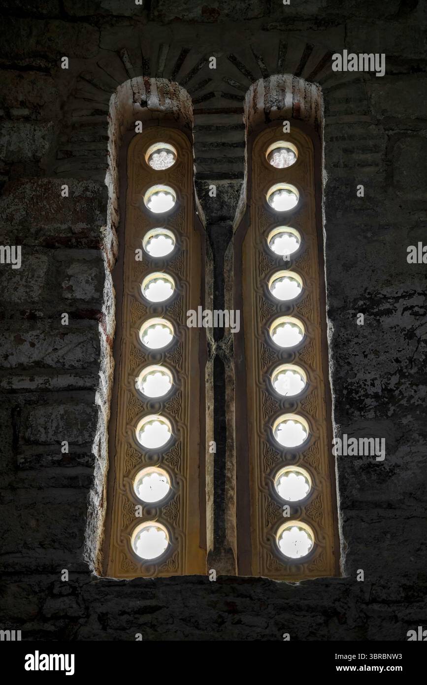 Primo piano di una stretta finestra bizantina presso il Sacro Monastero di Dafni in Grecia, con inserti circolari in vetro e muratura in pietra. Foto Stock