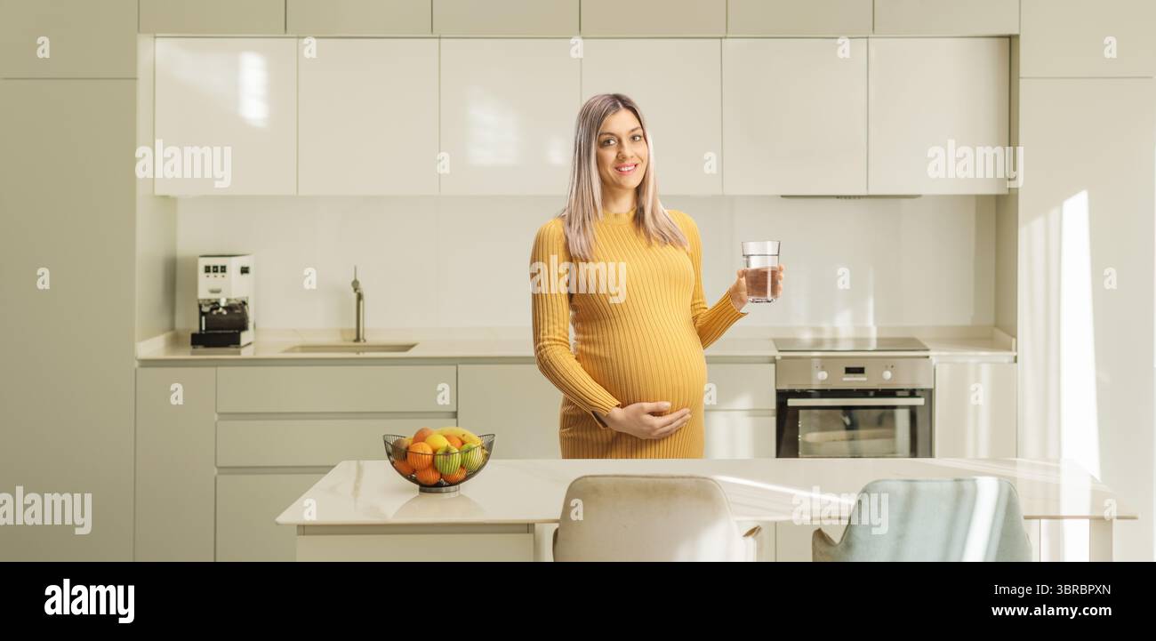 Donna incinta che tiene un bicchiere d'acqua in cucina Foto Stock