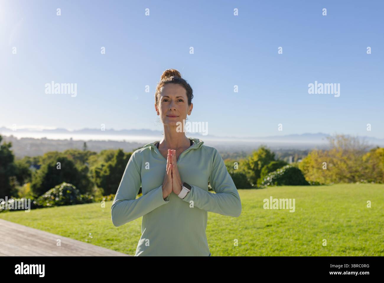 Donna che pratica yoga con abbigliamento atletico con smartwatch sul ponte che si affaccia sulle montagne all'alba Foto Stock