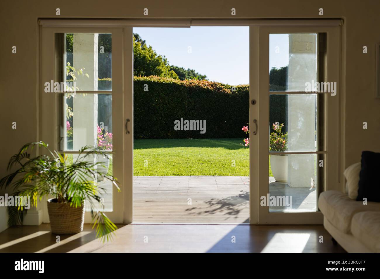 Porte scorrevoli in vetro che si aprono e rivelano un patio in legno con prato verde sotto la luce del sole Foto Stock