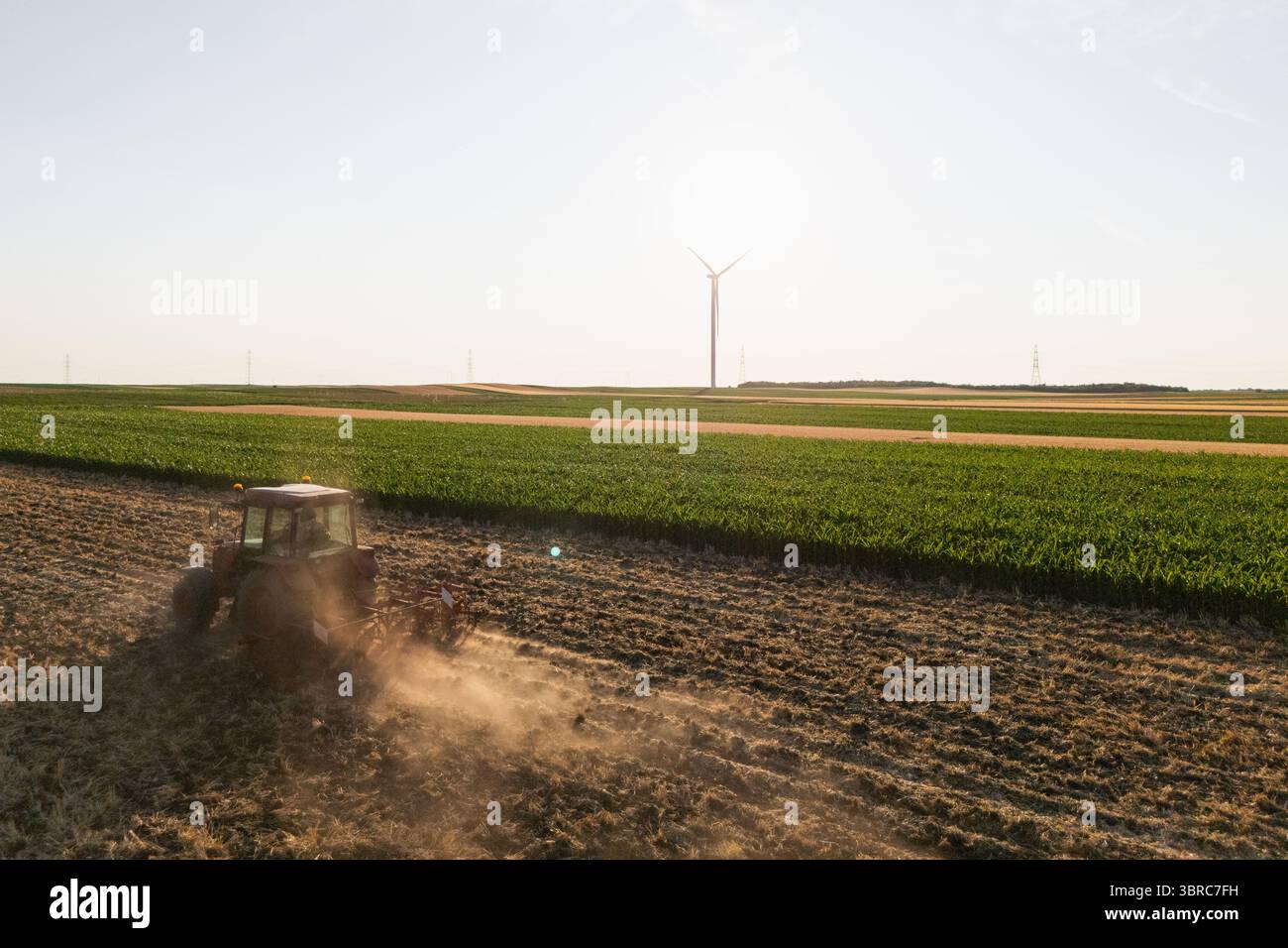 Il trattore agricolo lavora sul campo con turbine eoliche. Vista aerea. Foto Stock Il trattore agricolo lavora sul campo con turbine eoliche. Vista aerea. Foto Stock