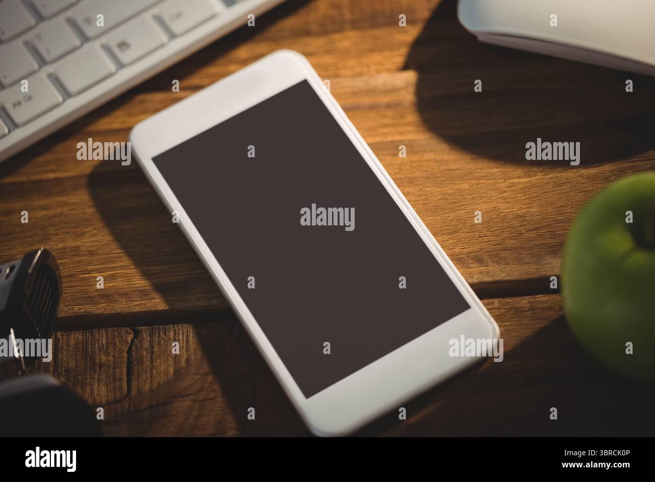 Il design piatto mostra lo smartphone bianco appoggiato su una scrivania in legno con tastiera, mouse, mela verde Foto Stock