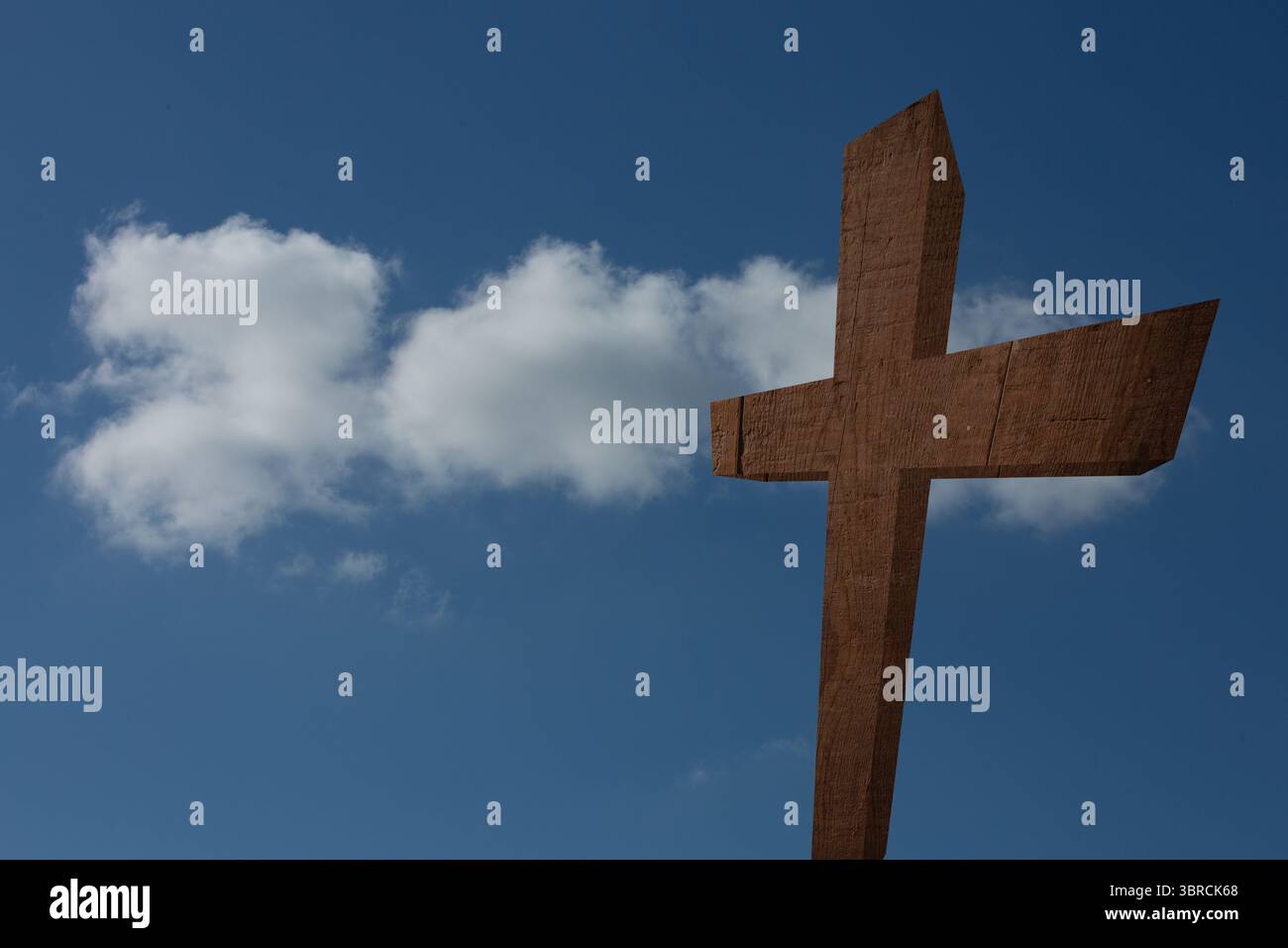 La croce in legno sgrossata si erge contro un cielo blu limpido con nuvole bianche alla deriva in un design piatto Foto Stock