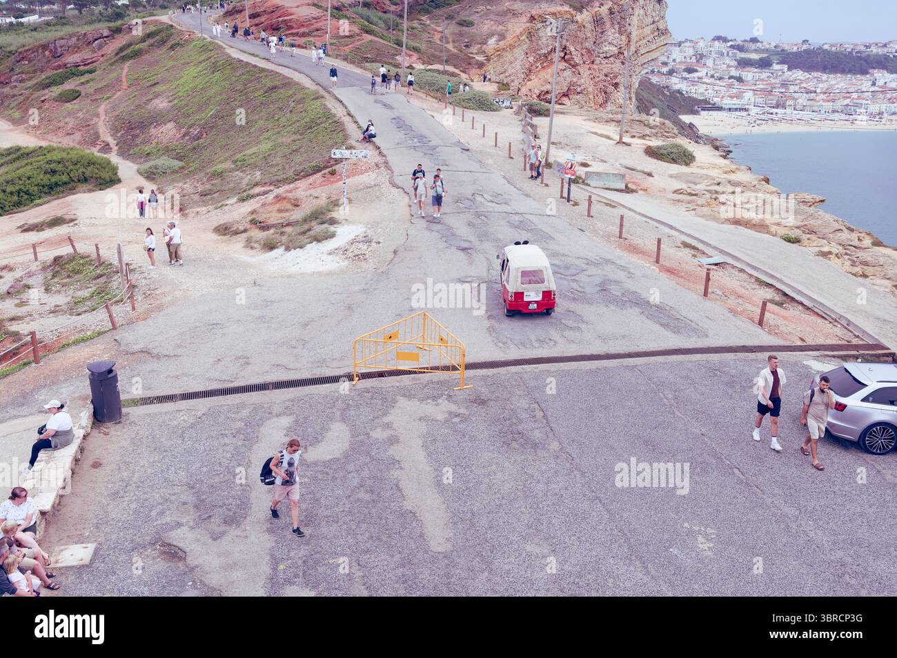 I turisti camminano e fanno un giro in tuk tuk lungo l'aspra strada costiera vicino alle scogliere di Nazaré Foto Stock