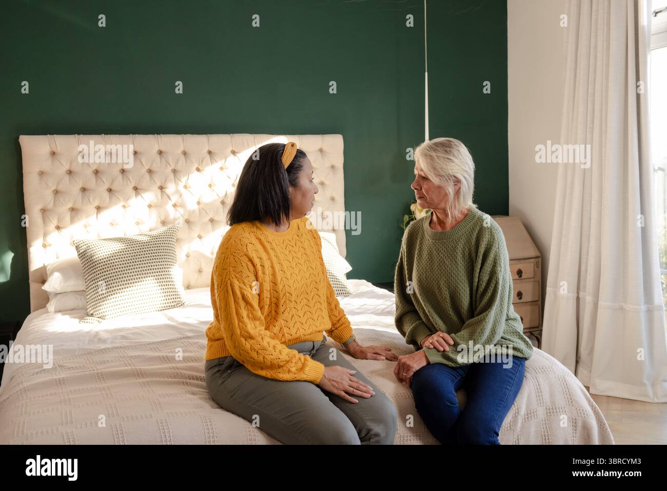 Diverse amiche si siedono sul bordo del letto in camera da letto con testiera in tufo e cuscino di lancio Foto Stock