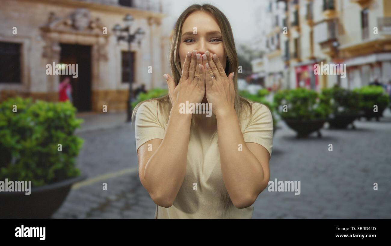 Donna sorridente e baciata alla macchina fotografica in una vivace scena di strada cittadina caratterizzata da architettura classica e vegetazione lussureggiante. Foto Stock