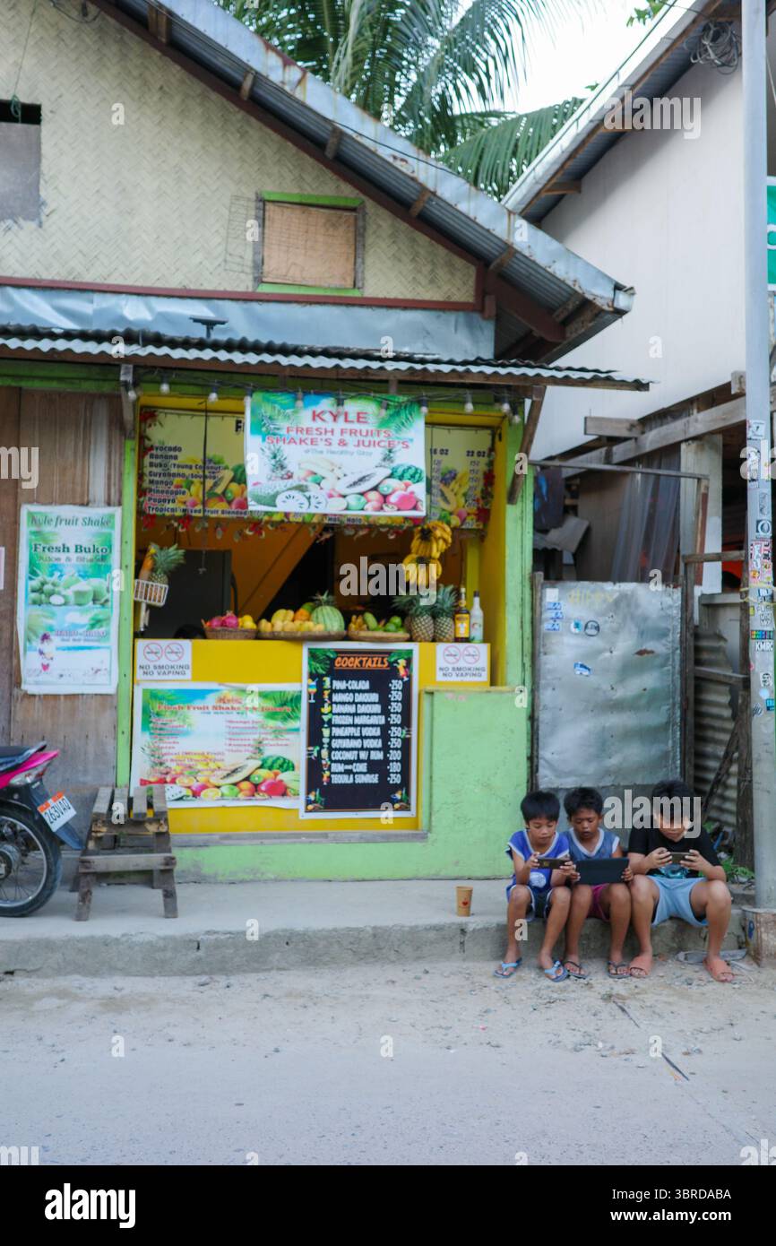 Un gruppo di tipi che giocano insieme di fronte a un negozio di Street food locale, vendendo frutta fresca e frullati a Palawan, Filippine Foto Stock