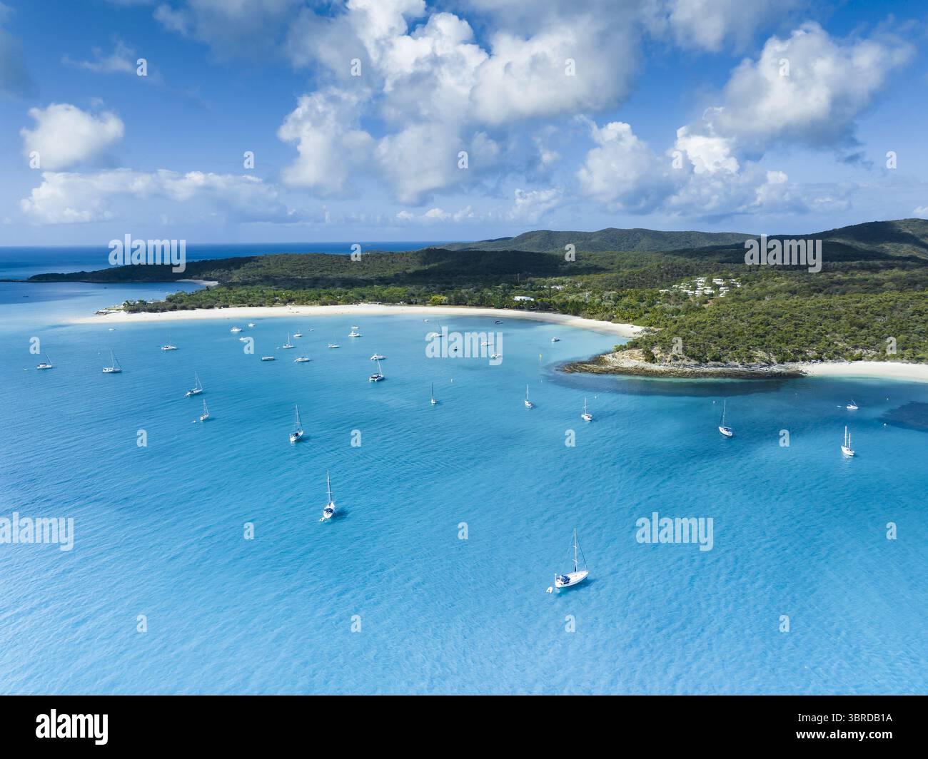 Vista aerea delle acque turchesi abbracciano le incontaminate sabbie bianche di Whitehaven Beach, punteggiate da barche a vela sotto un cielo di nuvole soffici, Queensland, Australia. Foto Stock