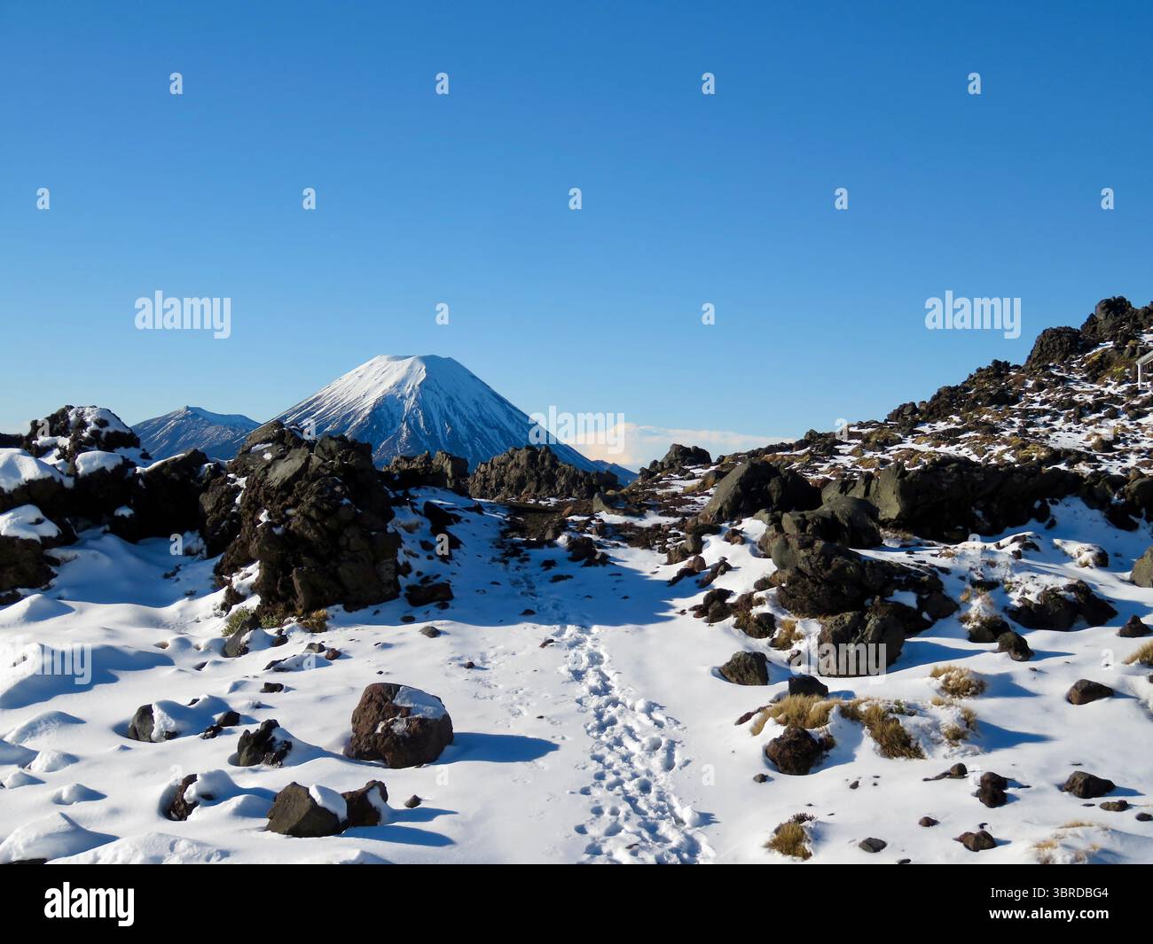 Le impronte di neve fresca conducono attraverso una silenziosa valle vulcanica verso il Monte Ngauruhoe, il Parco Nazionale di Tongariro, nuova Zelanda. Foto Stock