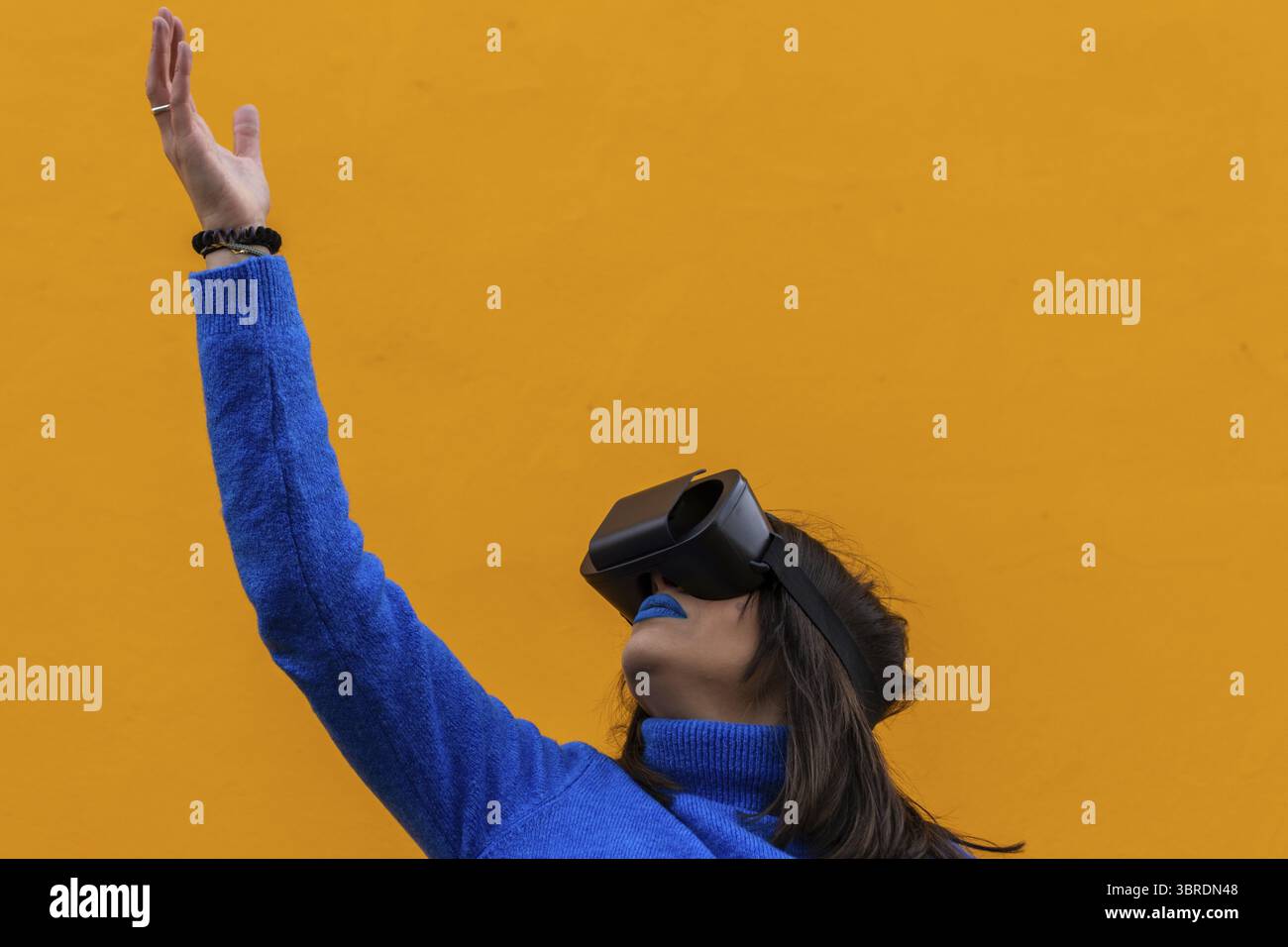 Ritratto isolato di una donna con abiti blu che indossano occhiali vr e toccano qualcosa di invisibile nella realtà virtuale. Sfondo giallo Foto Stock
