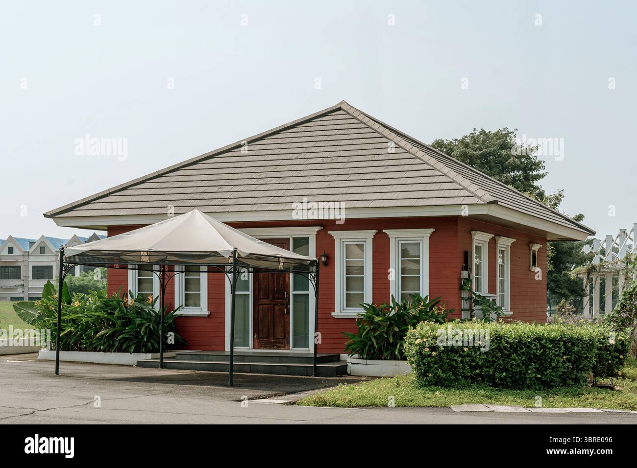 Giacarta, Indonesia, 12 luglio 2025. Un'affascinante casetta con pareti rosse, un tetto in piastrelle marroni e un bellissimo paesaggio. Una casa accogliente Foto Stock