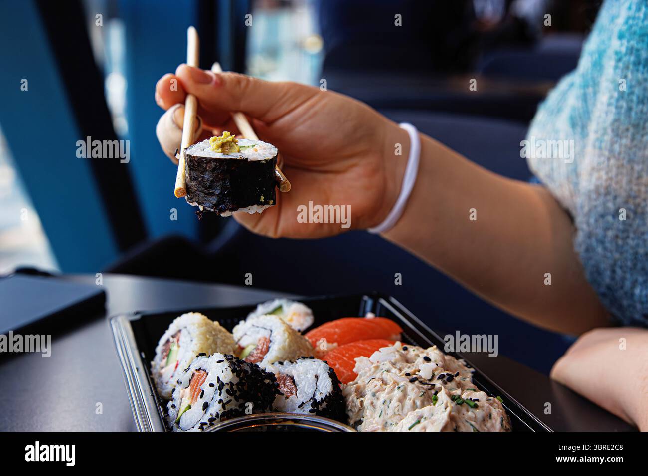 Primo piano della mano della persona che prende un rotolo di sushi con bacchette su un vassoio nero in un caffè moderno. Messa a fuoco selettiva Foto Stock