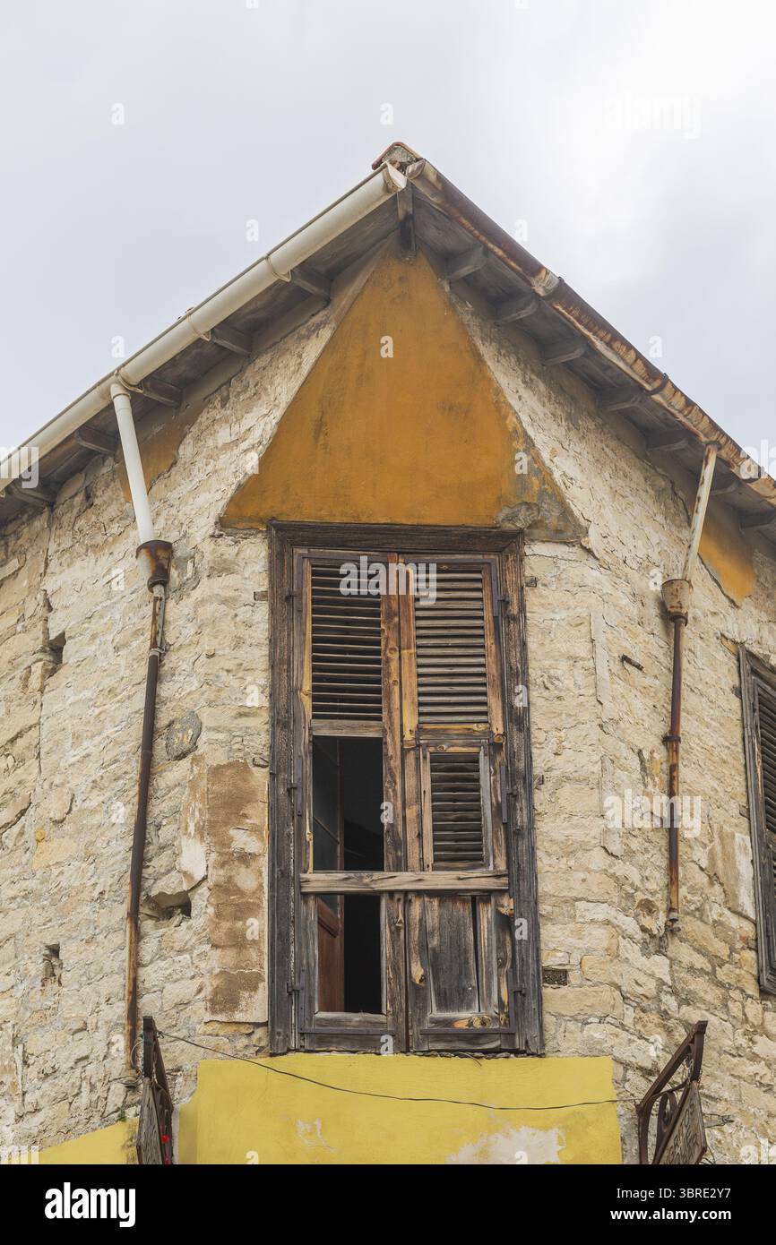 Vista dell'edificio in pietra intemprata con una porta in legno fatiscente e un accento ocra triangolare sotto un cielo nuvoloso a Limassol, Limassol, Cipro. Foto Stock