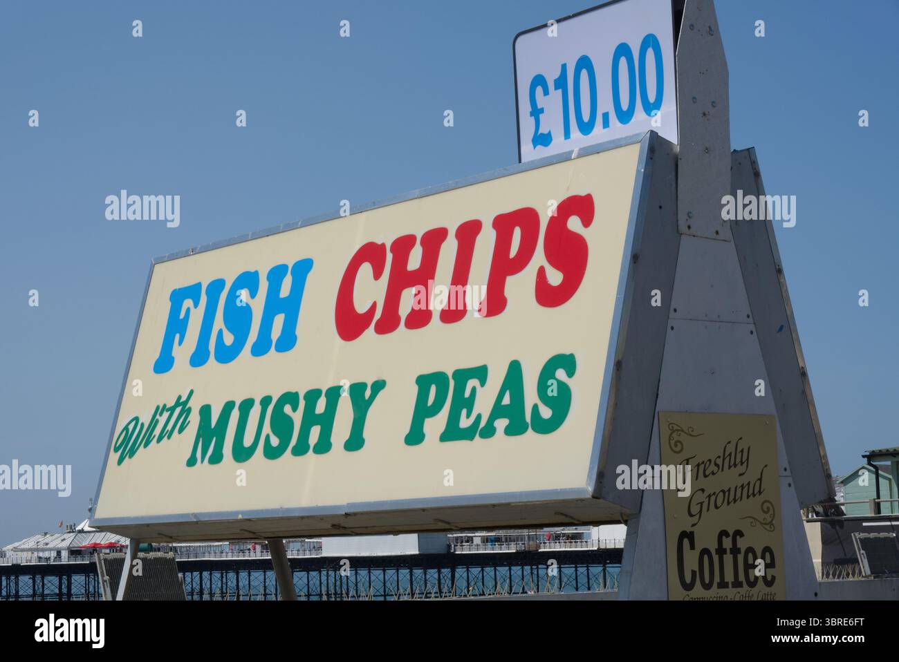Fish Chips con cartello Mushy Peas sul lungomare e sulla spiaggia di Brighton nell'East Sussex, Inghilterra. Molo sullo sfondo. Foto Stock
