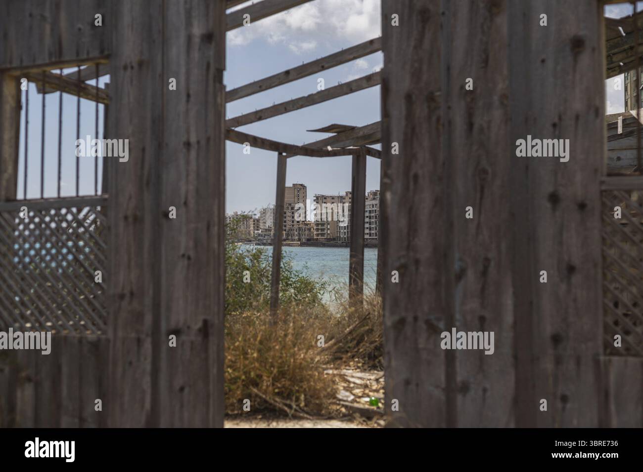 Veduta della decadente struttura in legno che incornicia la sagoma spettrale di edifici lontani attraverso acque scintillanti, una scena toccante, Varosha, Famagosta, Cipro. Foto Stock