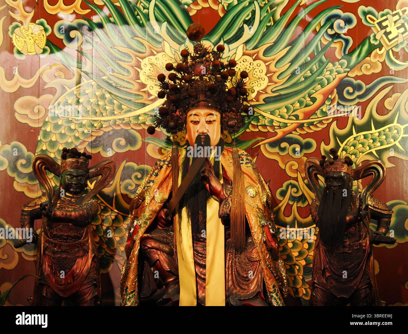 Taipei, Taiwan - 7 novembre 2024 - Una statua della divinità centrale riccamente ornata con una corona e una barba elaborate, fiancheggiata da due figure, posta contro un vib Foto Stock