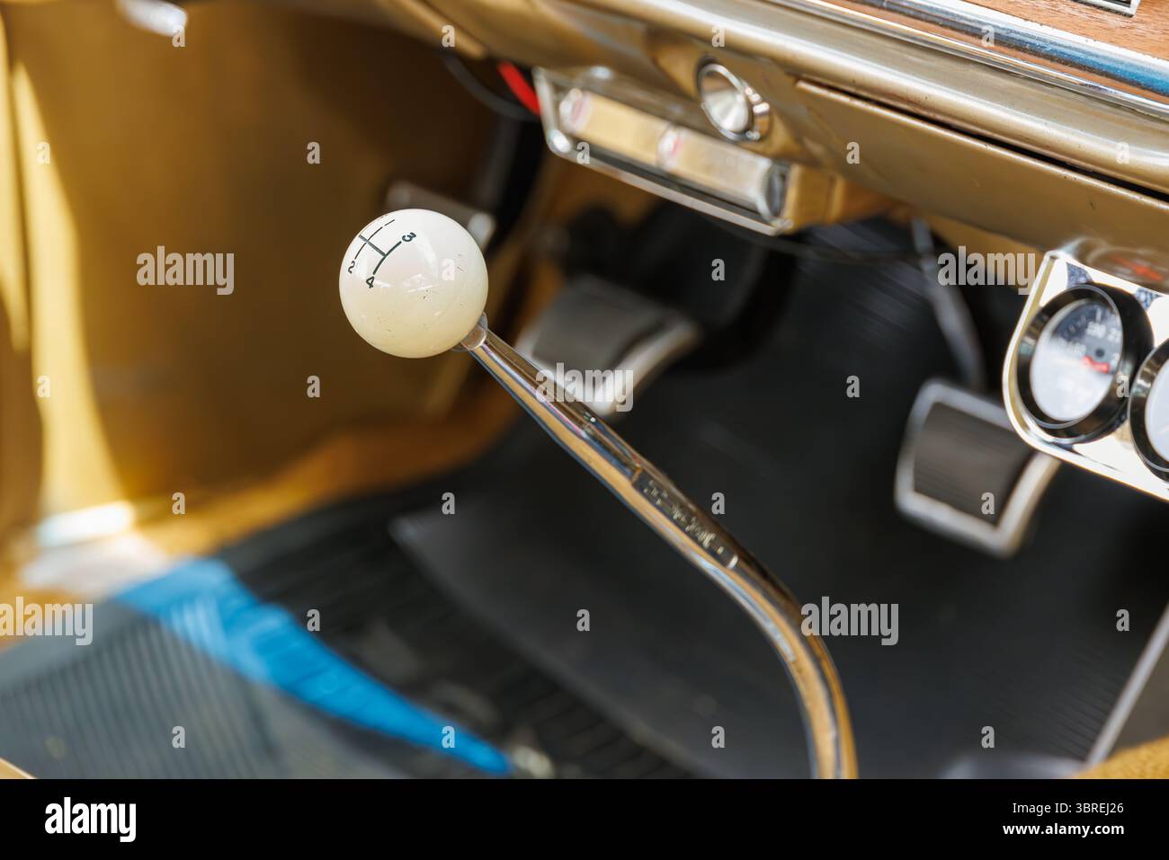 Primo piano del cambio manuale di un'auto d'epoca con manopola bianca, bastoncino cromato e set di pedali, che mostrano il classico design automobilistico con un'illuminazione calda. Foto Stock