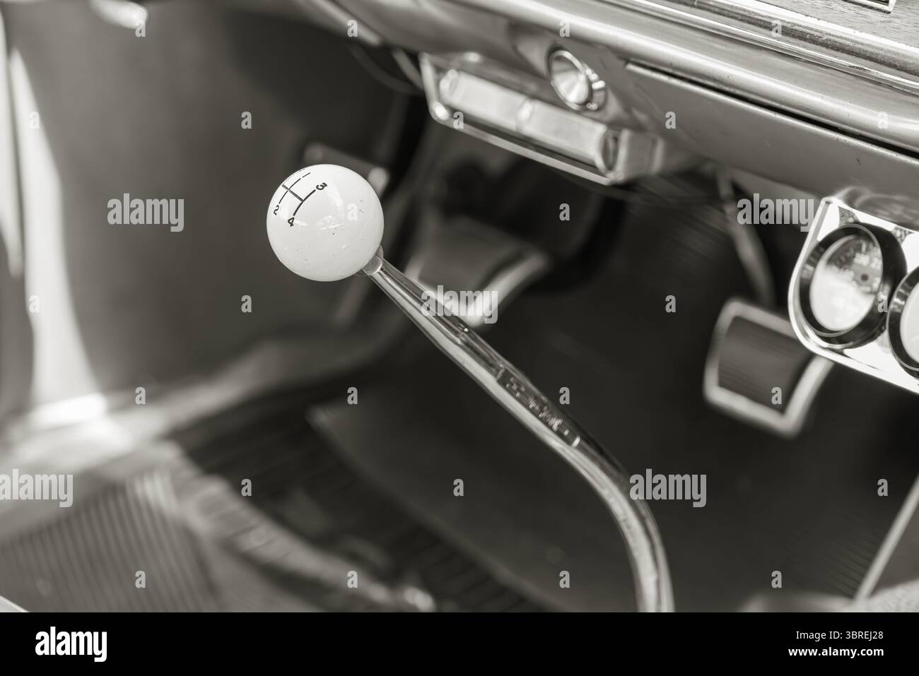 Primo piano in bianco e nero del cambio manuale di un'auto d'epoca con manopola bianca, pedali e cruscotto, per catturare il classico design automobilistico. Foto Stock