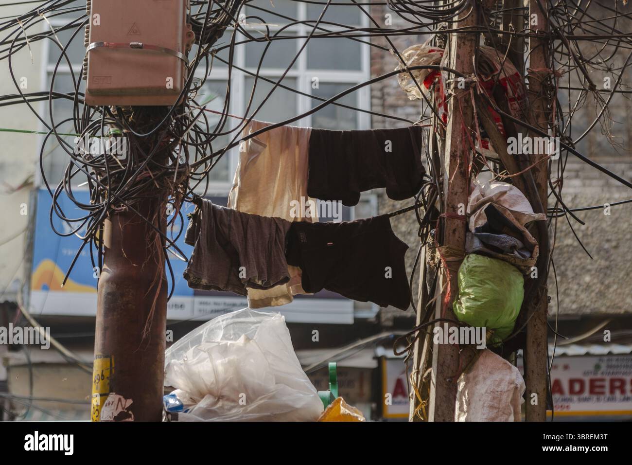 Vista della lavanderia appesa in una caotica rete di fili aggrovigliati su pali intemprati, in contrasto con il degrado urbano, nuova Delhi, Divisione di Delhi, India. Foto Stock