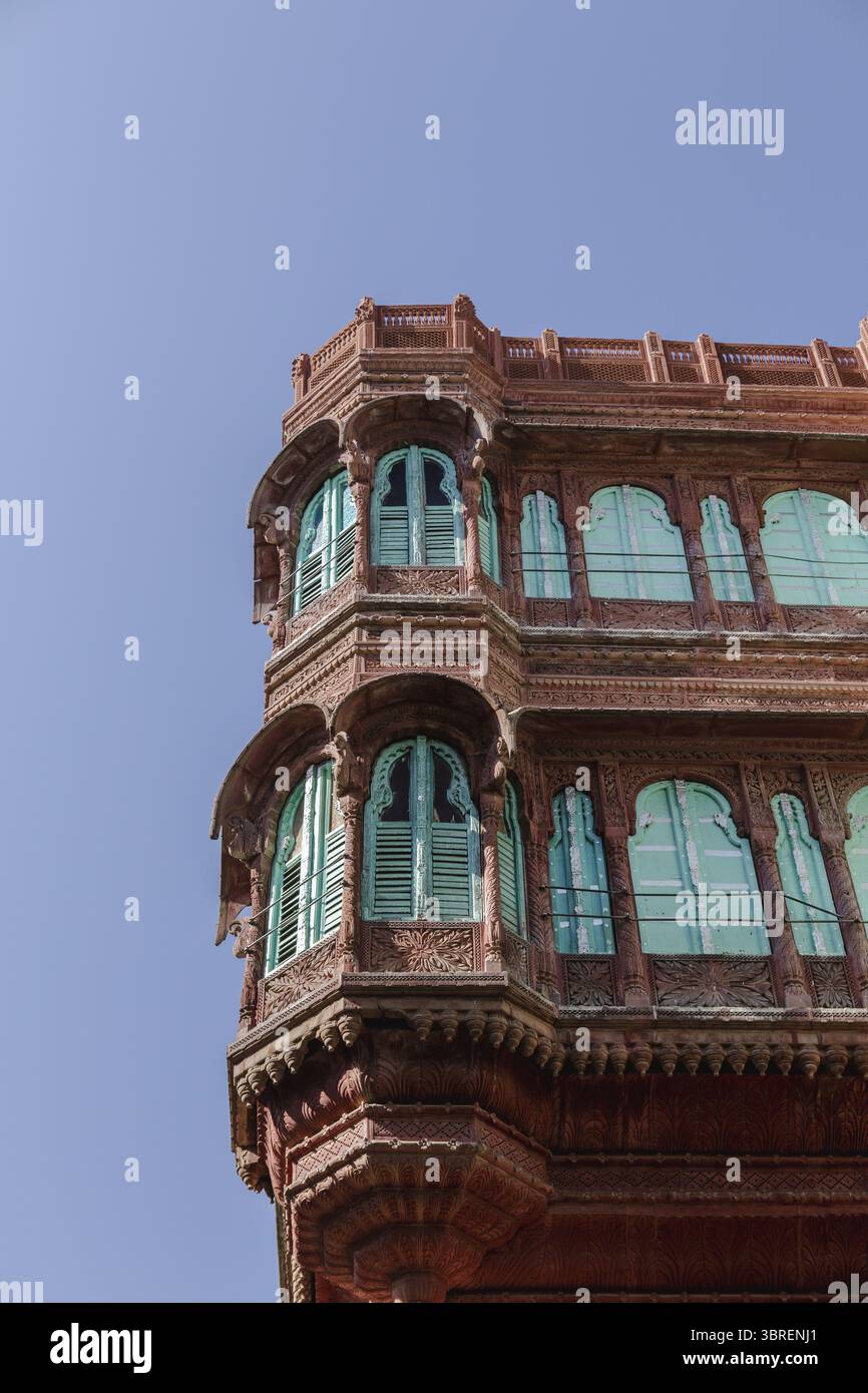Vista di un edificio ornato in arenaria rossa con finestre turchesi che contrastano con un cielo azzurro, che mostra intricati dettagli architettonici, Bikaner, Rajasthan, India. Foto Stock