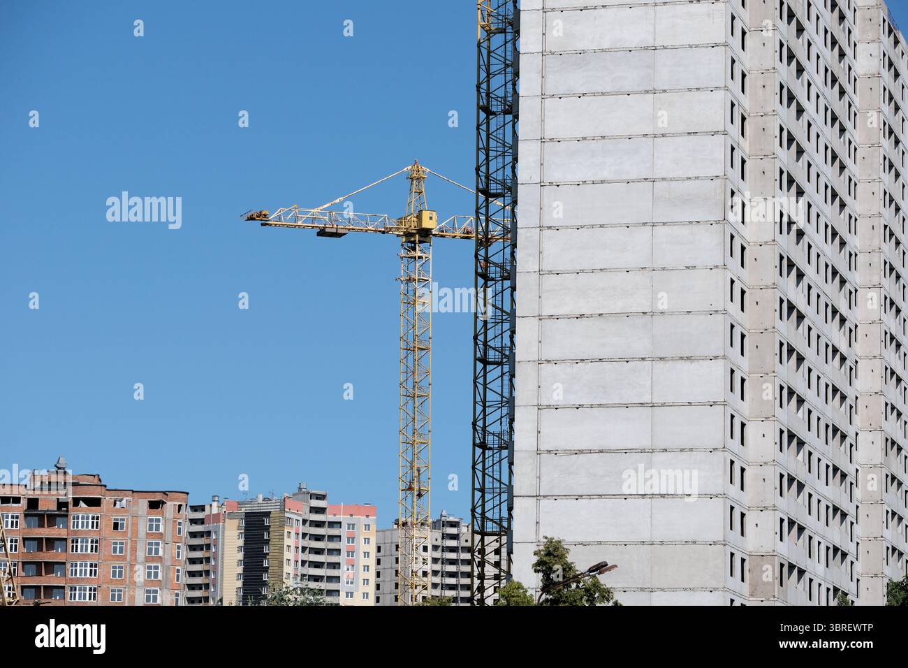 Una gru alta lavora diligentemente accanto a un edificio in cemento in costruzione. Foto Stock