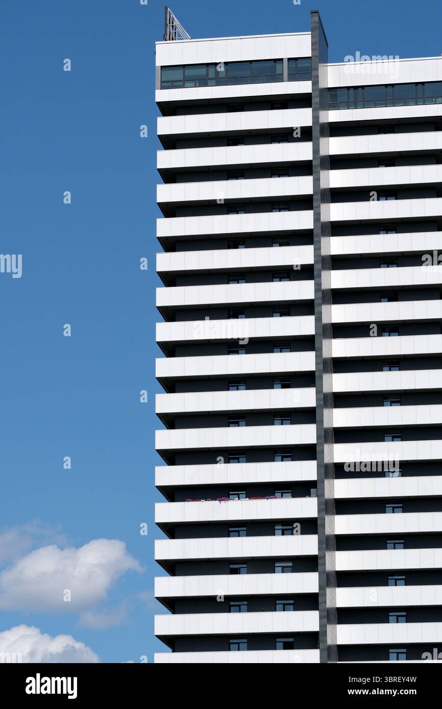 Alto edificio con distintive strisce bianche raggiunge l'alto sotto un luminoso cielo blu. Foto Stock