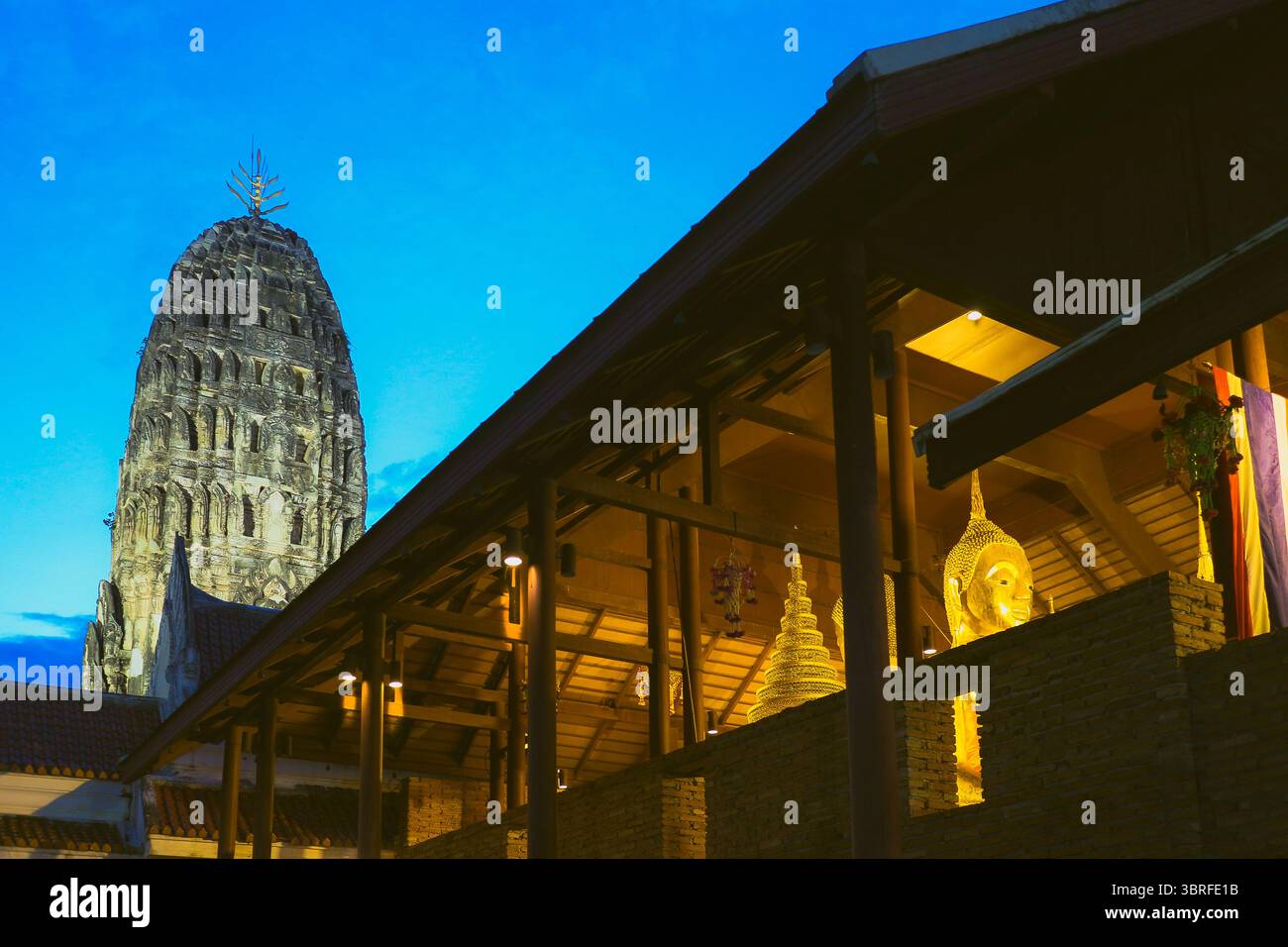 Patrimonio culturale Wat Mahathat Worawihan, Ratchaburi, Thailandia. Statua del Buddha in luce dorata al tramonto, con i chedi Dvaravati e il cielo blu al crepuscolo. Foto Stock