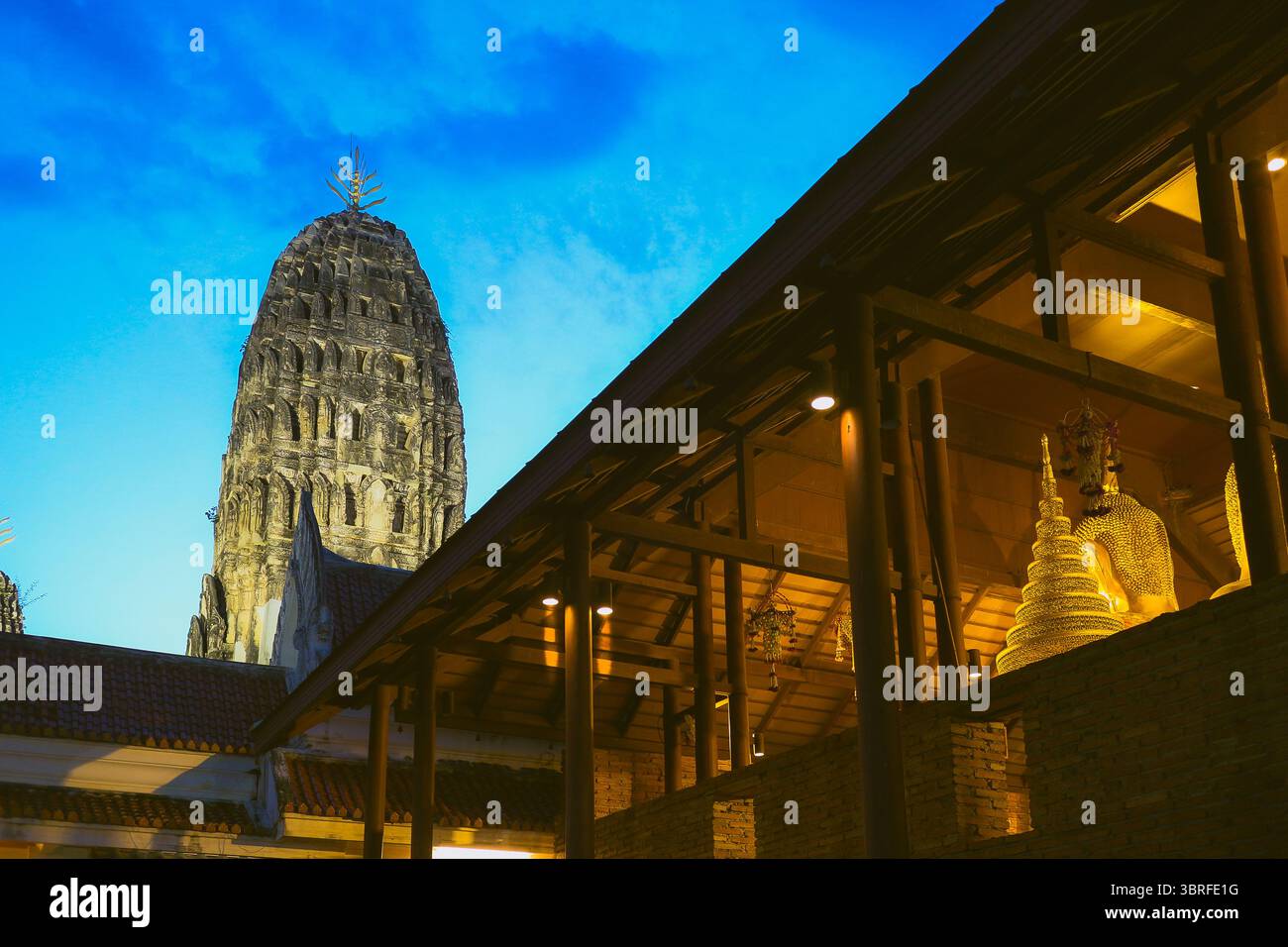 Calma spirituale Wat Mahathat Worawihan Ratchaburi, Thailandia. Testa di Buddha illuminata dalla luce del tramonto, antico chedi dietro sotto il cielo crepuscolo. Foto Stock