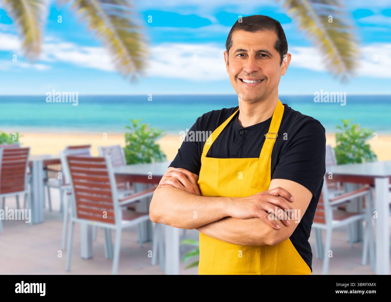 Bell'uomo che indossa un impiegato con grembiule al Beach hotel. Sorridendo con le braccia incrociate esprimendo emozioni positive Foto Stock