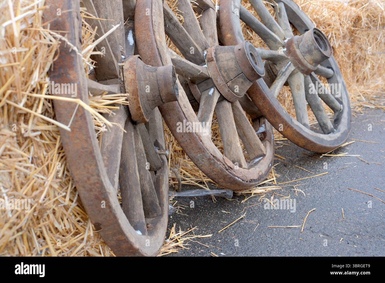 Le vecchie ruote in legno si appoggiano su un fieno sotto la luce soffusa del mattino. Foto Stock