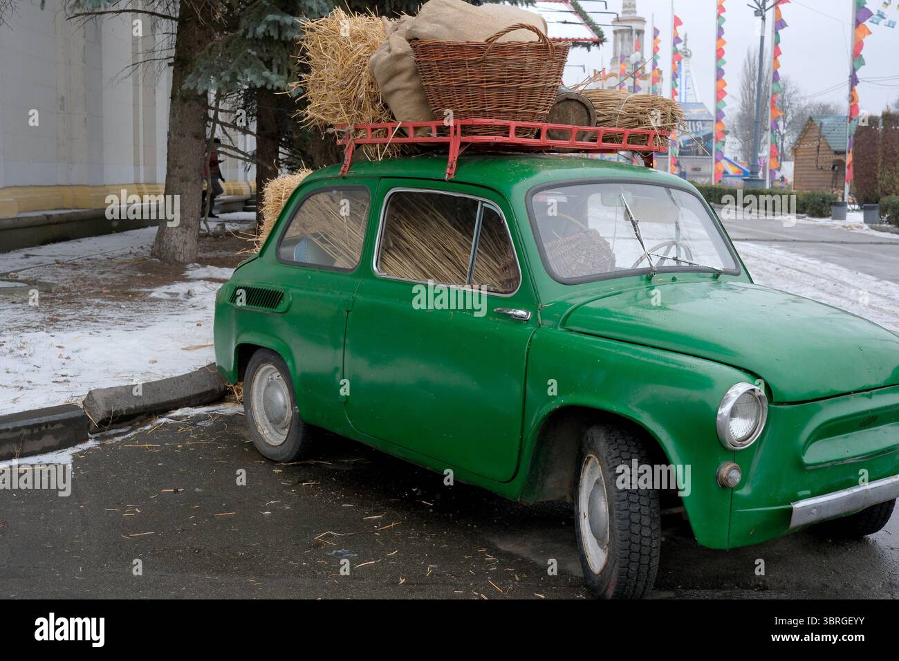 Una vivace auto verde è parcheggiata con un cesto di fieno sul tetto. Foto Stock