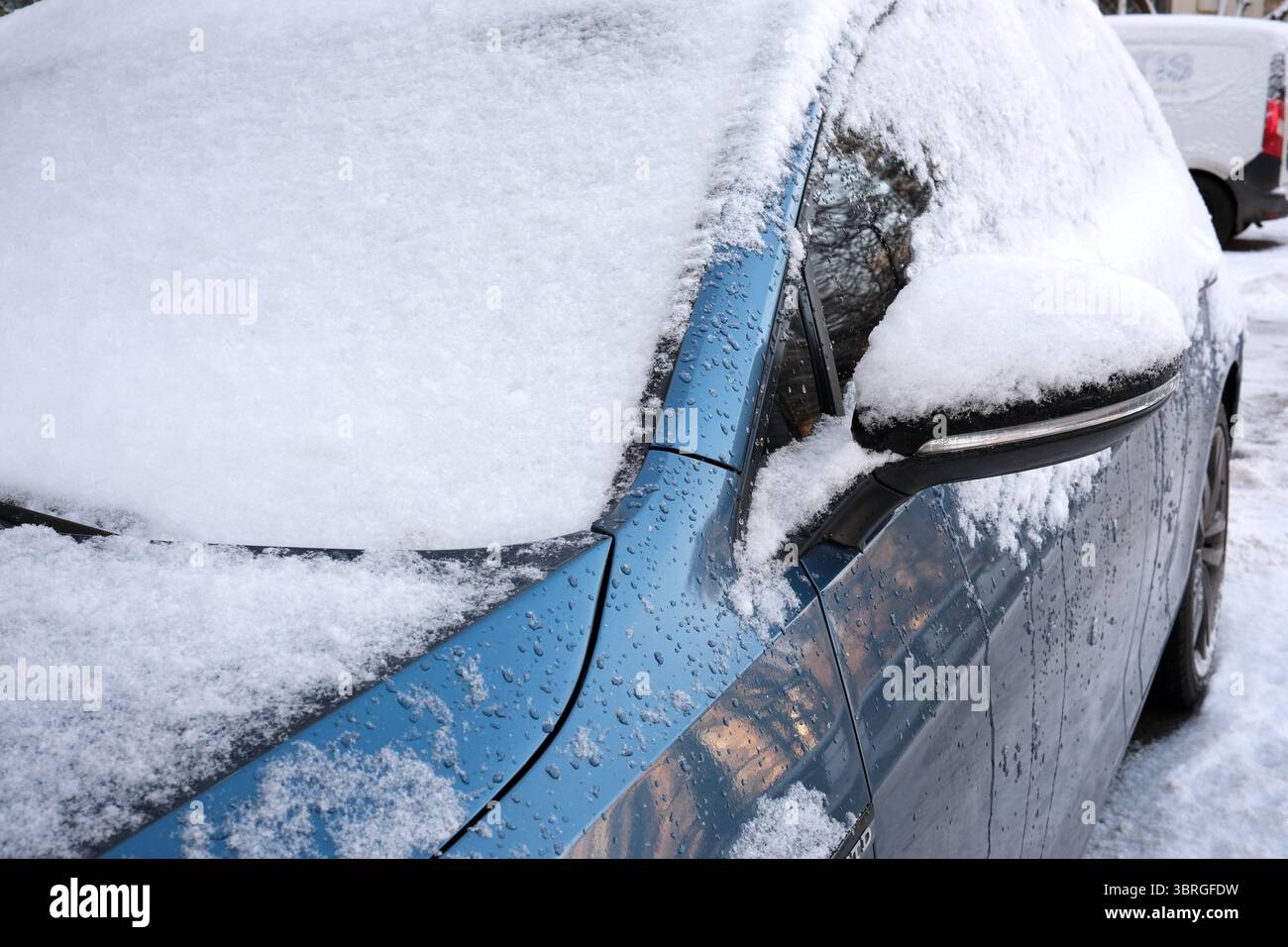 Una fitta neve copre un'auto blu brillante parcheggiata all'aperto in una giornata fredda. Foto Stock