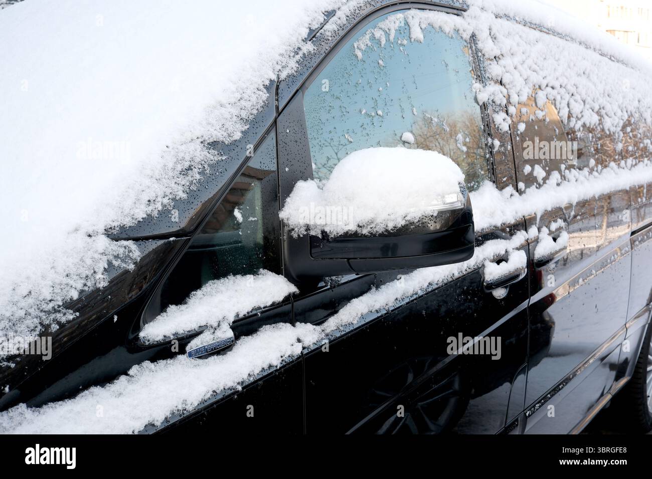 La neve copre un elegante veicolo nero parcheggiato in una tranquilla area urbana. Foto Stock