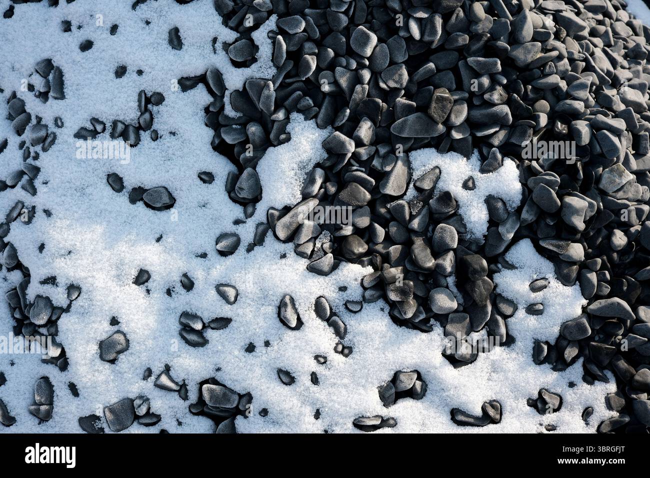 Pietre nere giacciono sparse sotto una morbida coperta di neve fresca. Foto Stock