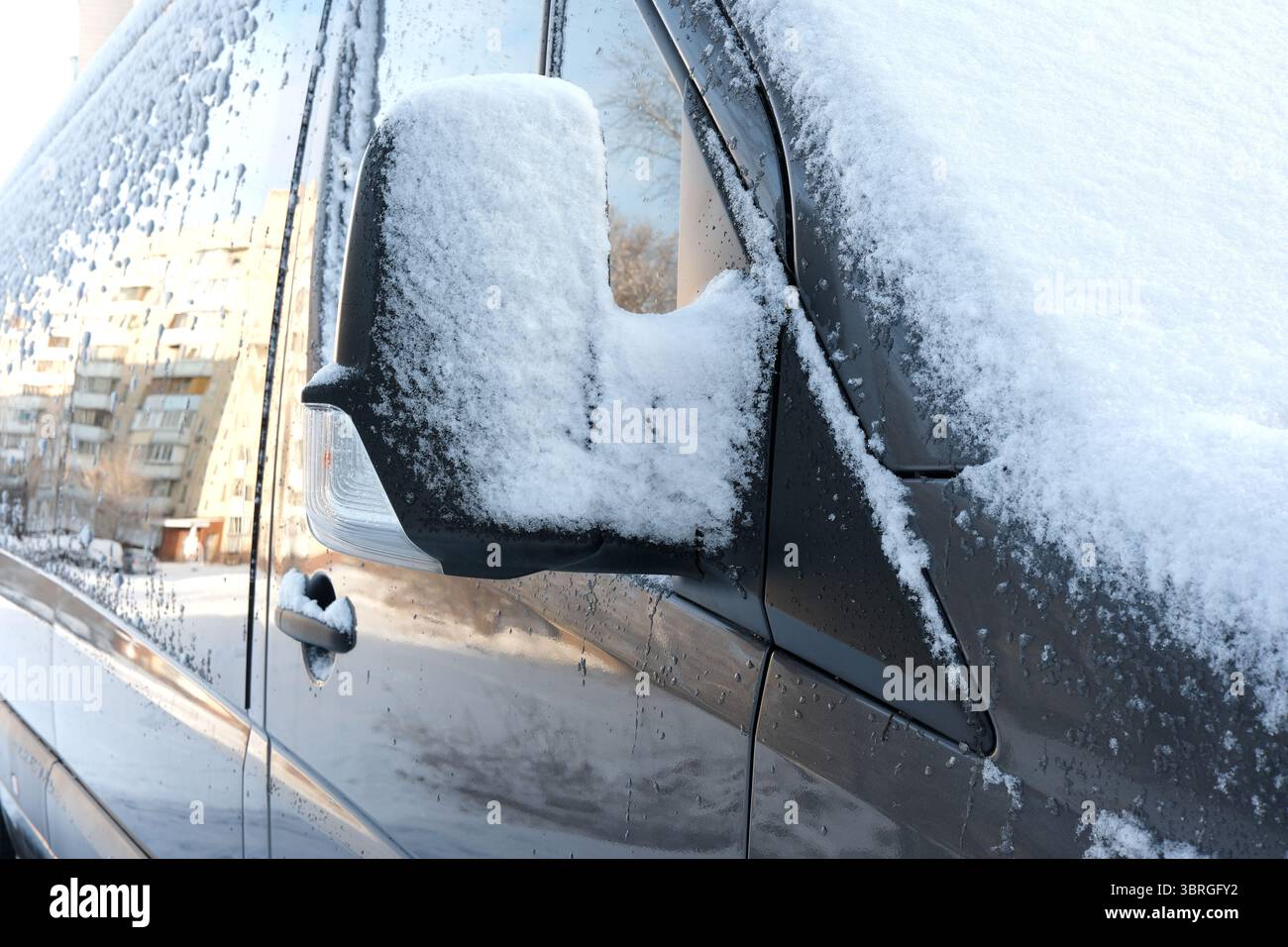 Le soffici coperte di neve avvolgono lo specchio di un'auto in una fredda mattinata invernale. Foto Stock