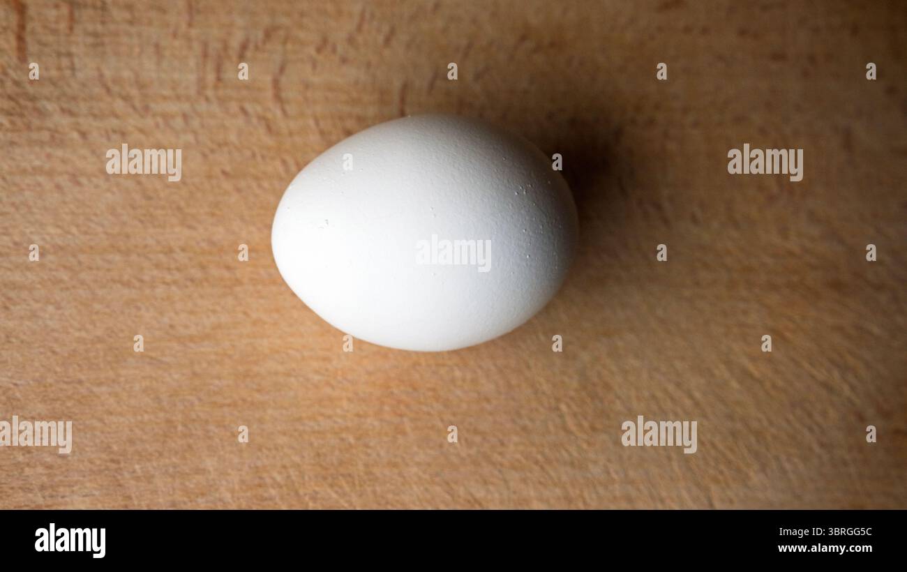 Un uovo bianco immacolato giace su una calda superficie di legno, pronto per la magia culinaria. Foto Stock