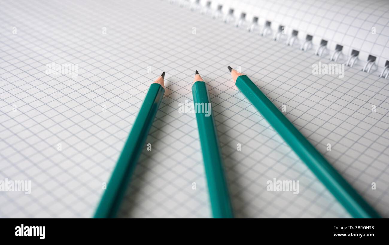 Tre matite verdi poggiano su una pagina quaderno a scacchi, pronte per la creazione. Foto Stock