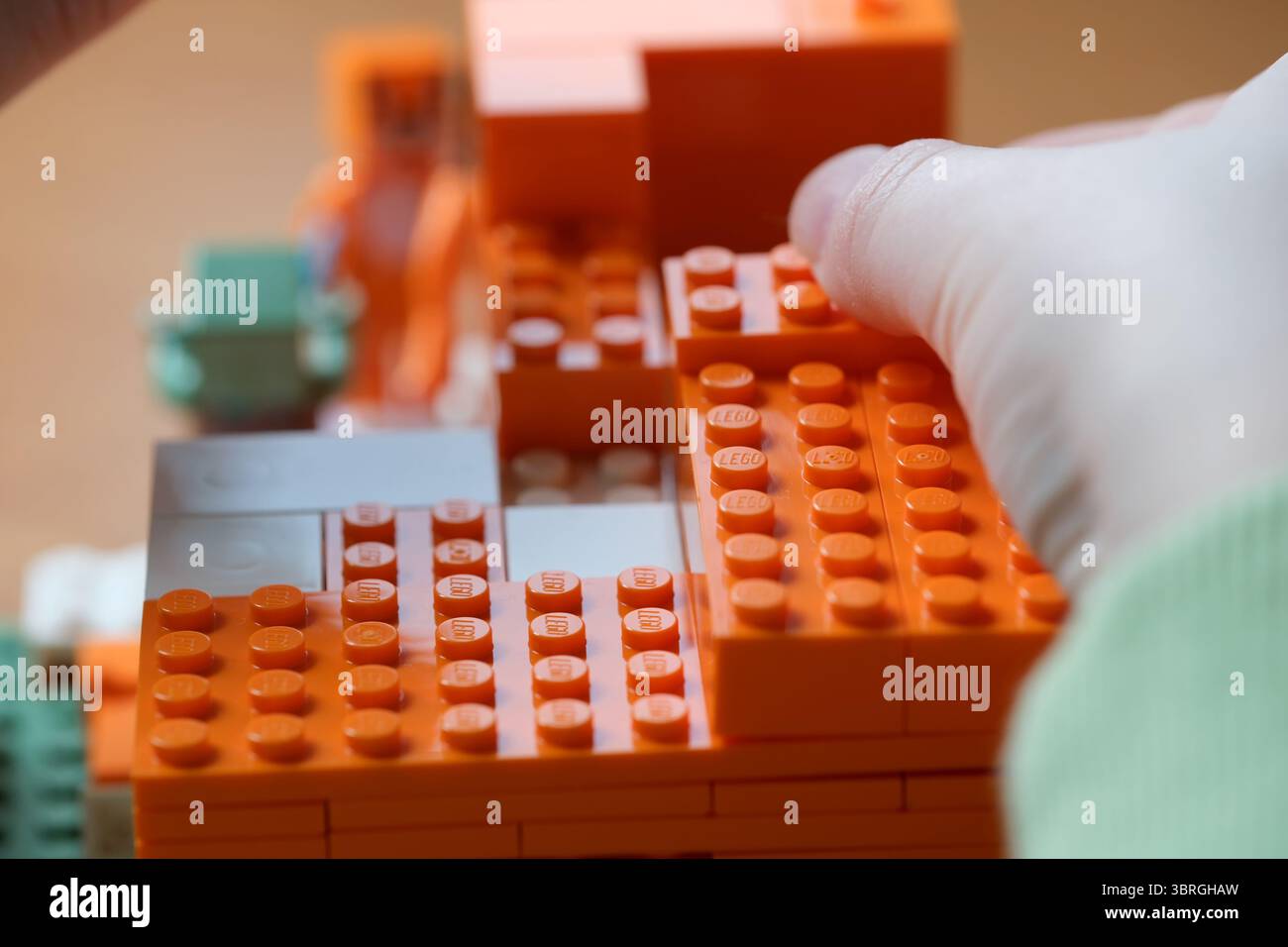 Le mani assemblano abilmente blocchi vivaci in una costruzione giocosa. Foto Stock