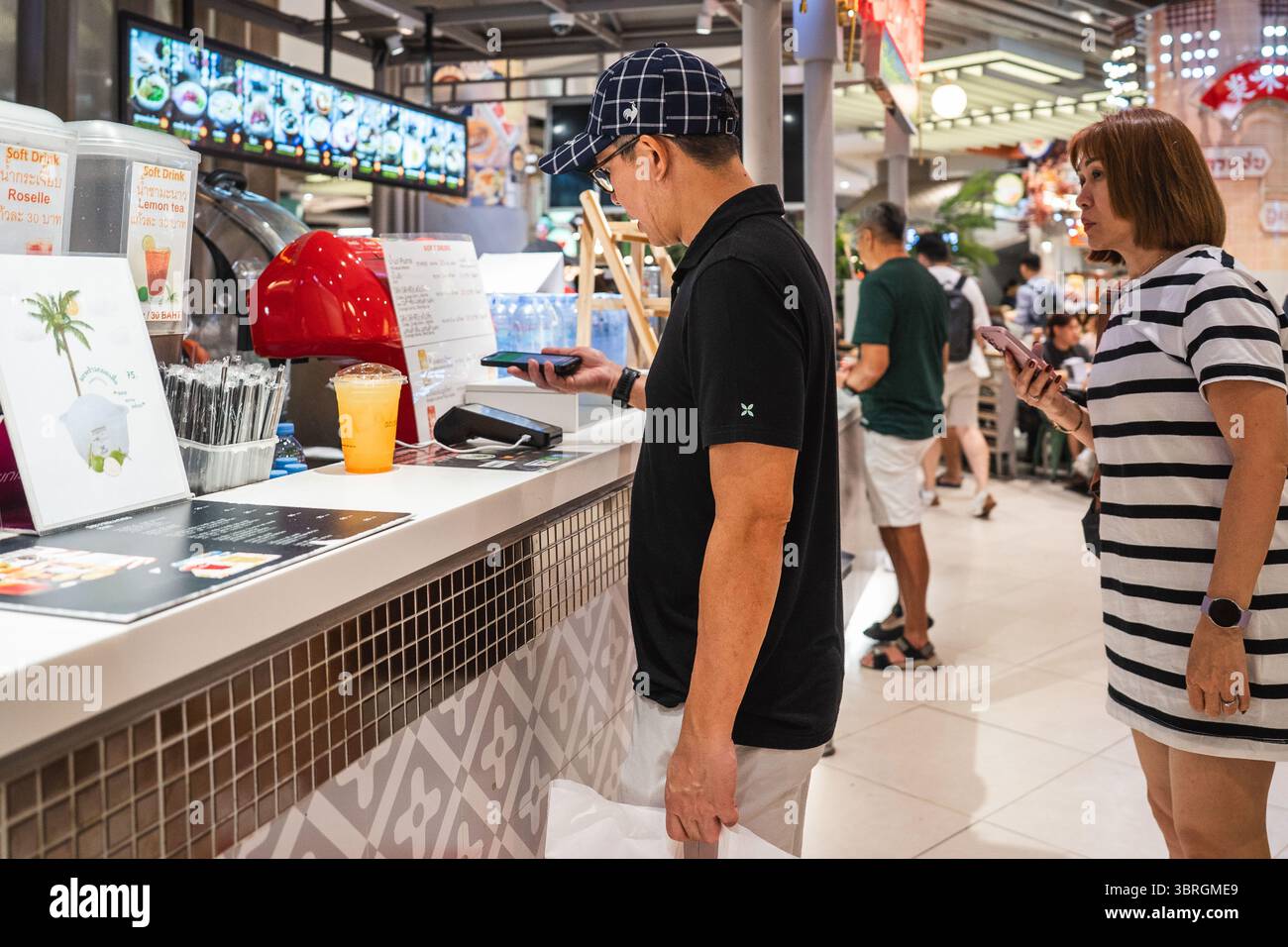 Bangkok, Thailandia. 12 luglio 2025. Un cliente esegue la scansione di un codice QR per pagare un drink in un chiosco all'interno dell'area ristoro di un centro commerciale. Loghi e vetrine dei marchi all'interno delle zone di lusso, bellezza, intrattenimento e gastronomia del Siam Paragon, uno dei centri commerciali più esclusivi di Bangkok. Le immagini documentano come il Visual branding definisca lo spazio retail contemporaneo. Credito: SOPA Images Limited/Alamy Live News Foto Stock