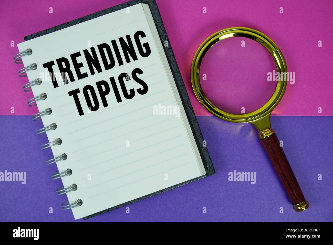 Argomenti di tendenza testo scritto su carta per notebook con lente di ingrandimento Foto Stock