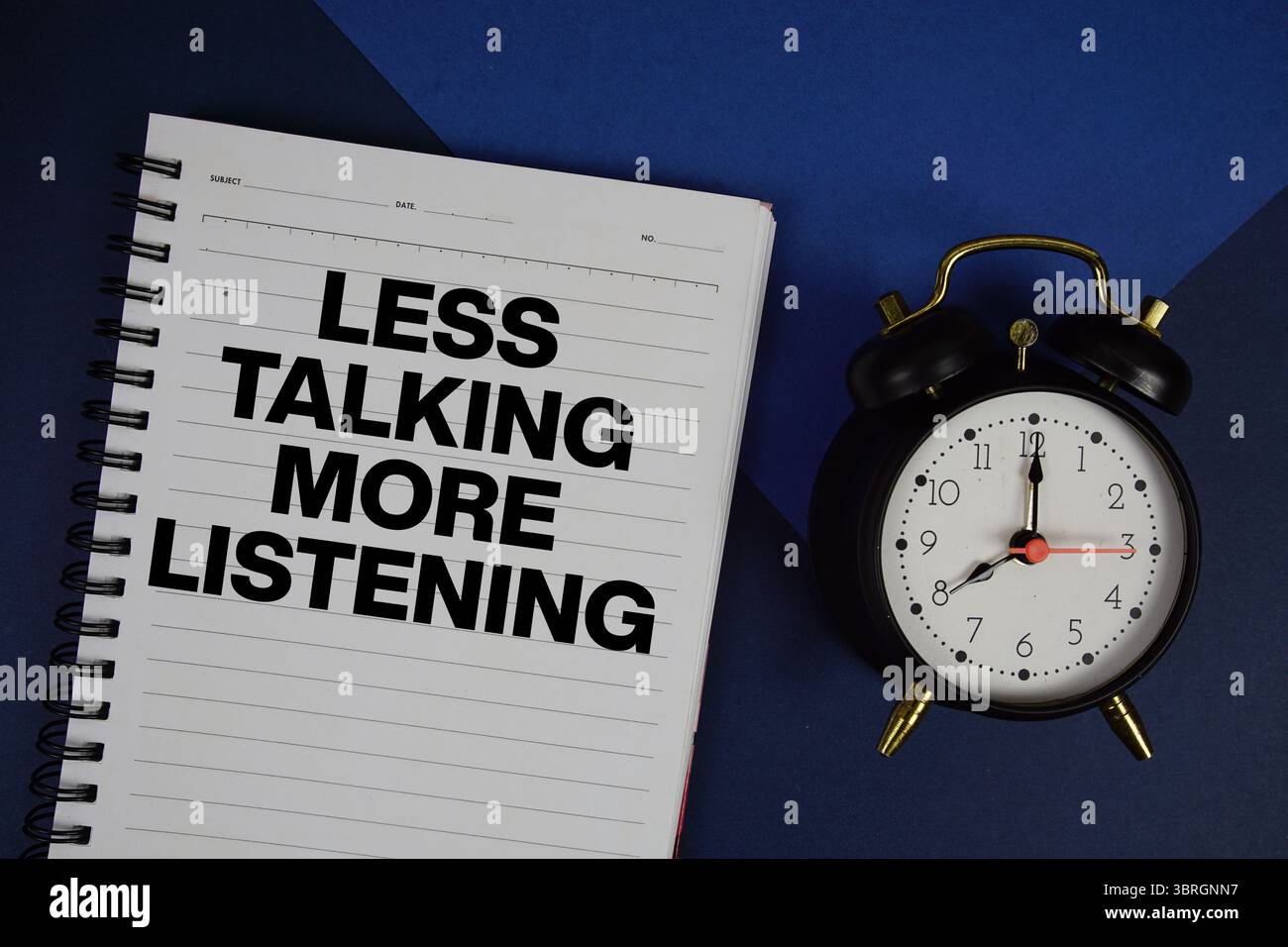 Meno chiacchiere più testo da ascoltare scritto sul blocco note con sveglia su sfondo blu navy Foto Stock