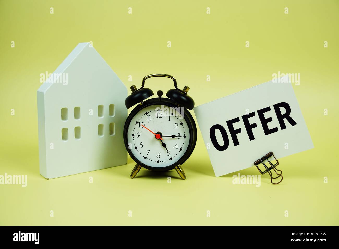 Testo con modello di casa e sveglia su sfondo giallo Foto Stock