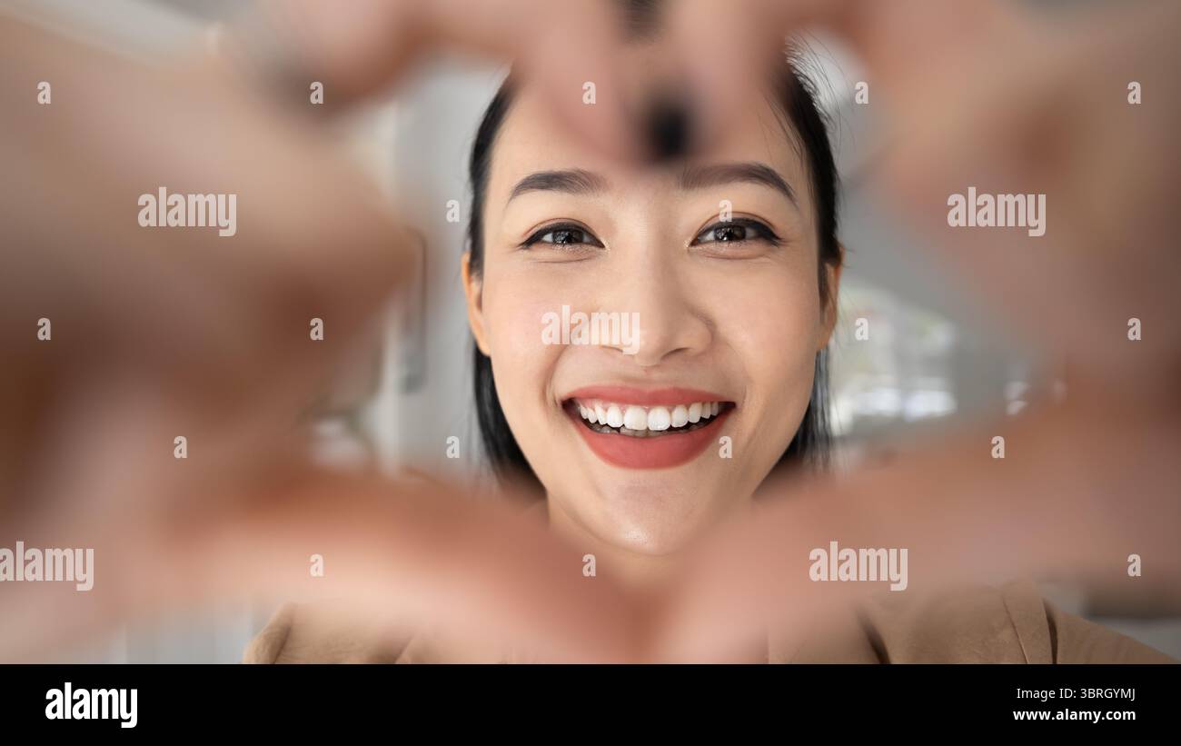 Donna asiatica che si mostra a macchina per un gesto a forma di cuore, primo piano Foto Stock